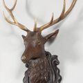 Tête de cerf en bois sculpté, yeux en verre sur écusson ouvragé. 